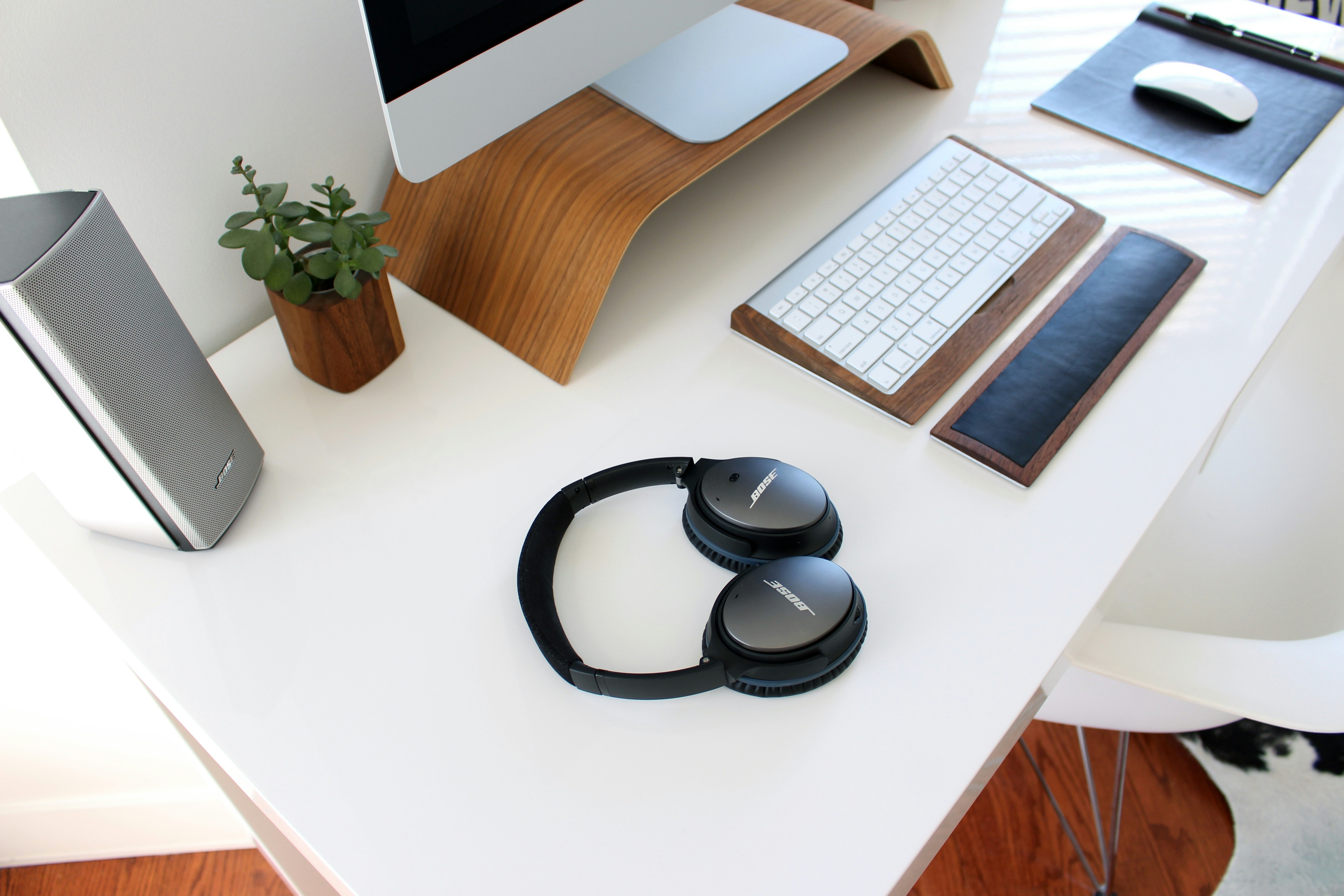 A desk with headphones, a keyboard and wrist wrest, monitor, mouse, speakers and a plant.